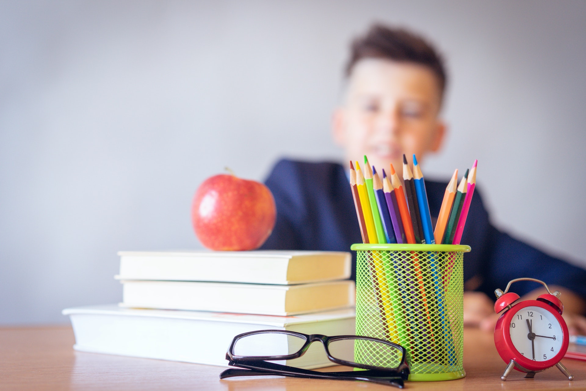A blurred student sits behind his school materials which include an apple and glasses.