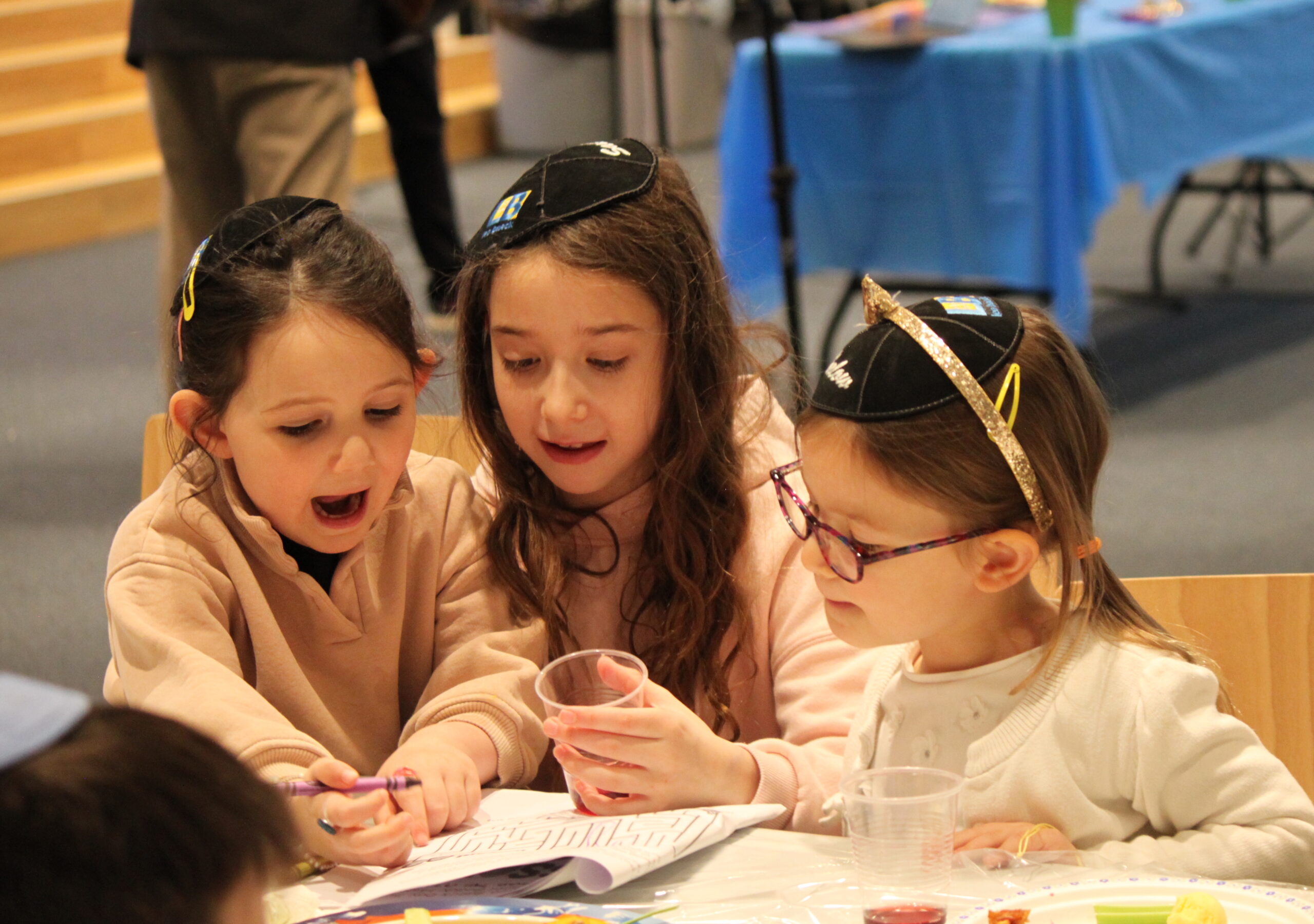 Three girls sitting closely together working on a maze together with crayons.