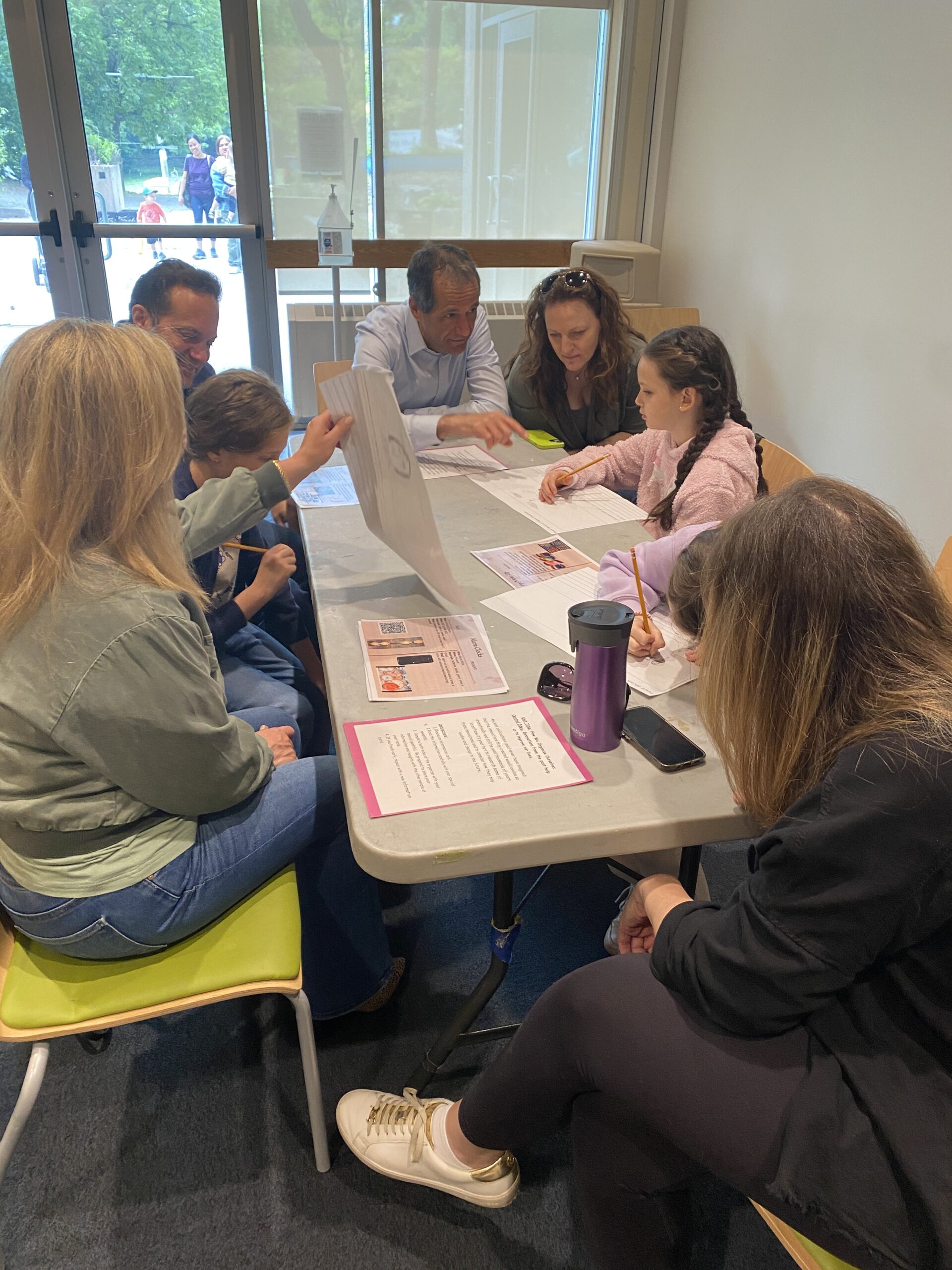 Parents and students gathered around a single table as they work individually on a worksheet.