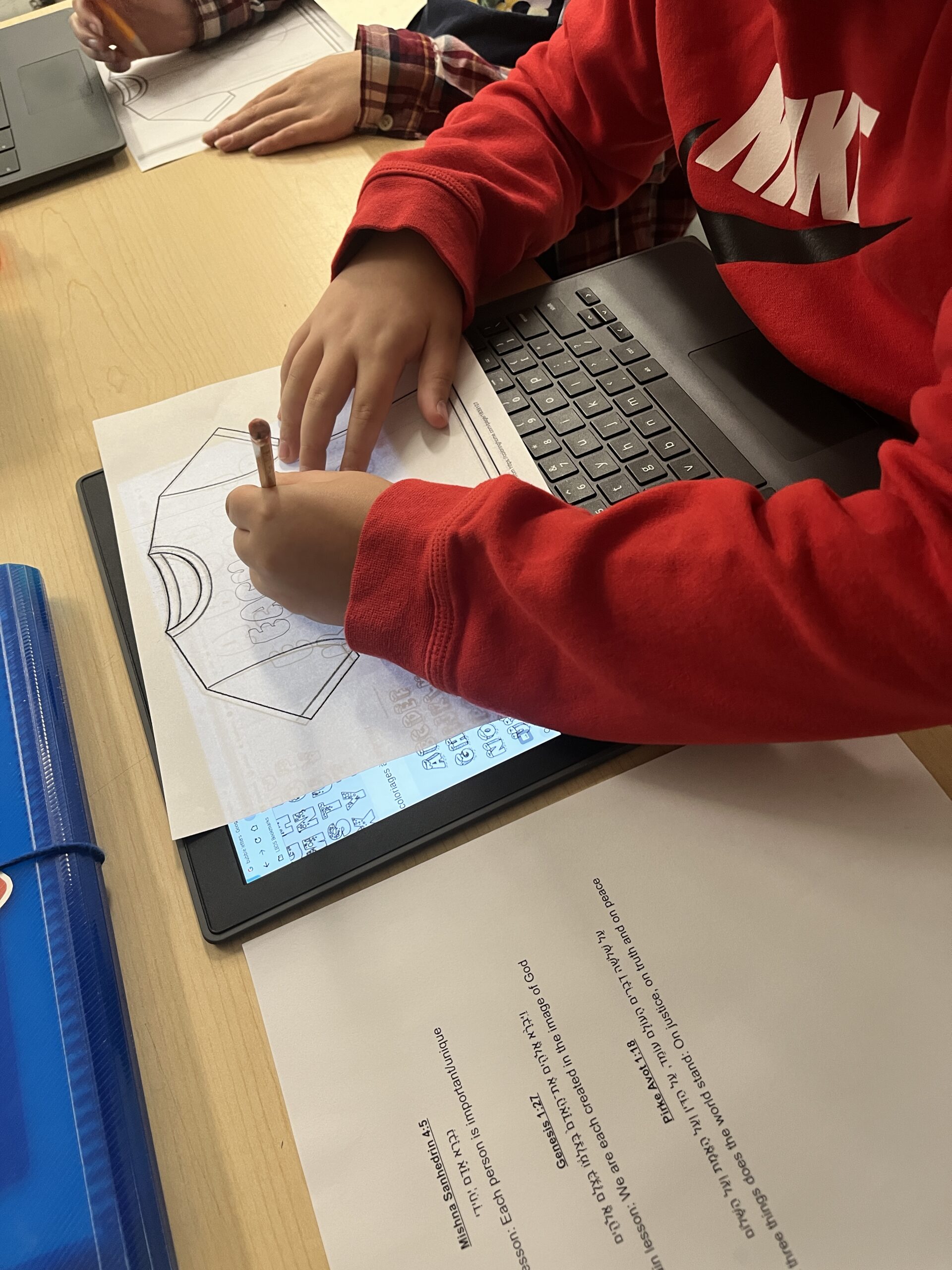 A student utilising a tablet to trace letters onto a drawing of a t-shirt.